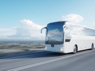 Ein weißer Bus fährt über eine Landstraße; im Hintergrund eine weitläufige Landschaft